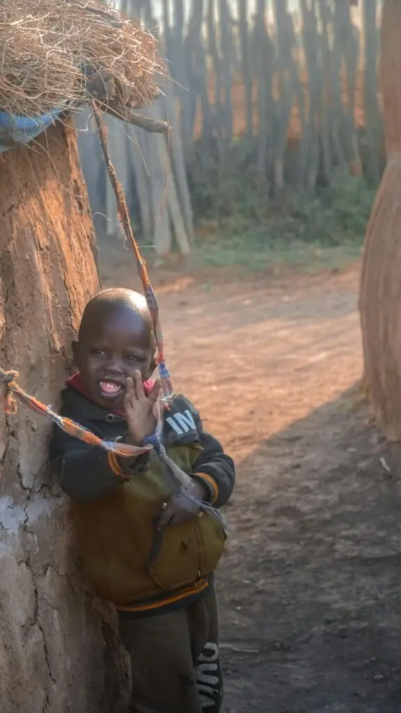 A joyful child playing near a traditional clay hut in rural Tanzania, captured in warm sunlight.